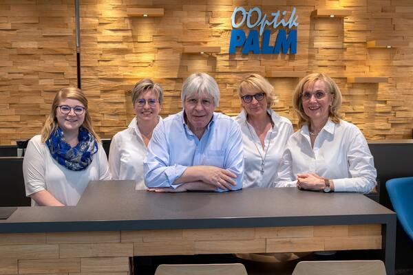 Team von Optik Palm mit fünf Mitarbeitern vor modernem Tresen im Optikergeschäft.