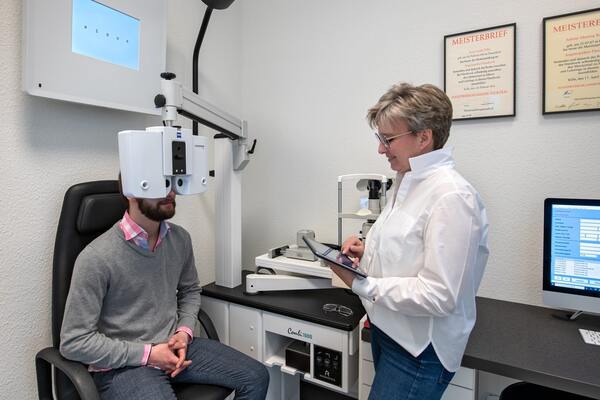 Augenoptikerin führt Sehtest mit moderner Augenmessung und Computer im Optikerladen durch.
